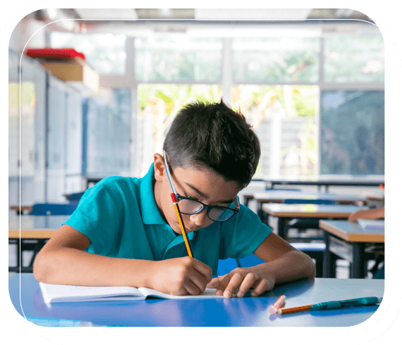 Boy sitting in a classroom working on an assignment in his notebook